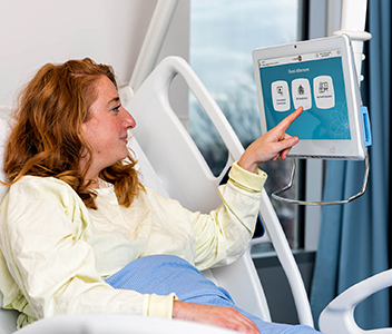 Patiente alitée en interaction avec un écran tactile suspendu